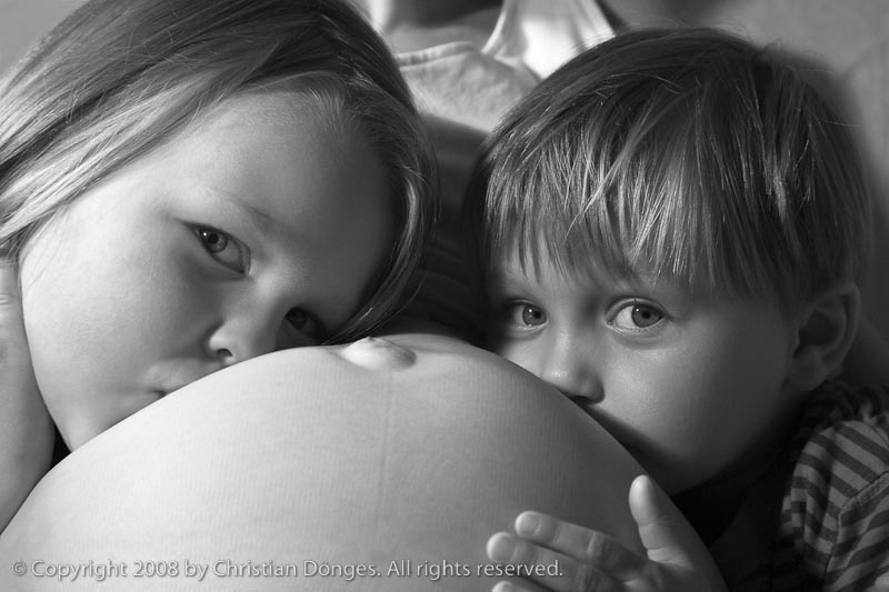 A boy and a girl are hugging their mother's belly containing their baby sibling.